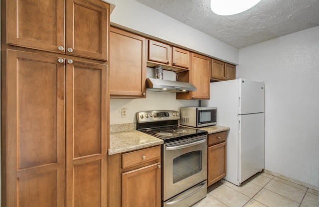 kitchen featuring exhaust hood, light tile patterned flooring, appliances with stainless steel finishes, a textured ceiling, and brown cabinetry