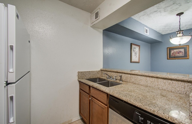 kitchen with a sink, dishwasher, brown cabinetry, freestanding refrigerator, and visible vents