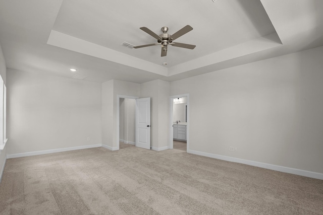 unfurnished bedroom featuring baseboards, light colored carpet, ensuite bathroom, and a raised ceiling
