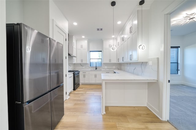 2420 Sumpter St, Houston, TX 77026 - kitchen featuring a sink, freestanding refrigerator, black range with gas stovetop, a peninsula, and white cabinetry