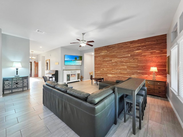 living area featuring wood finish floors, wood walls, an accent wall, ceiling fan with notable chandelier, and visible vents