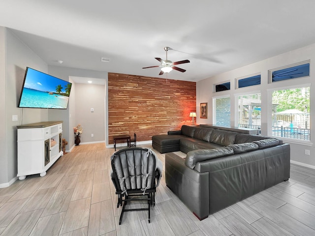 living room featuring wood finish floors, wood walls, an accent wall, a ceiling fan, and baseboards