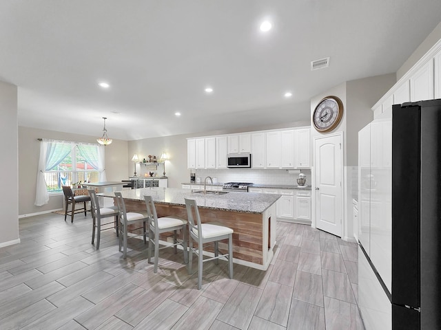 kitchen featuring a sink, stainless steel appliances, decorative backsplash, visible vents, and a center island with sink