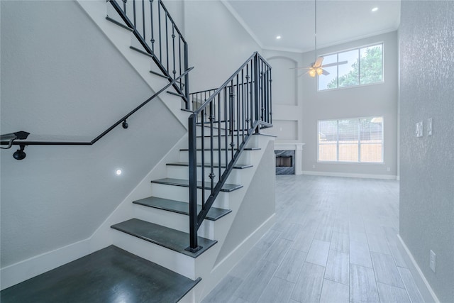 staircase with a textured wall, ceiling fan, a high ceiling, and a premium fireplace