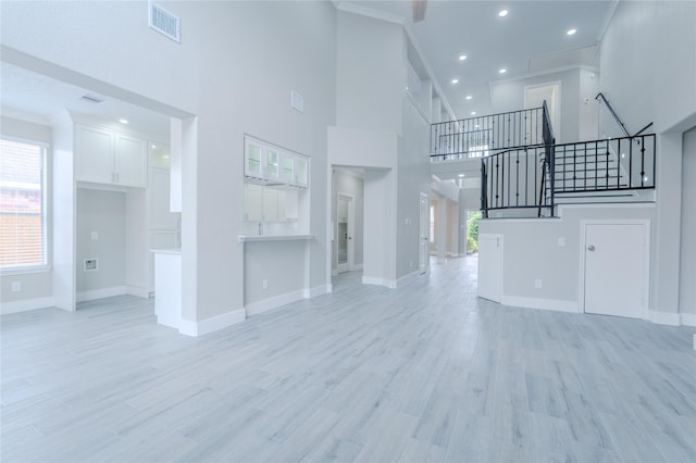 unfurnished living room with a high ceiling, baseboards, and light wood-style floors