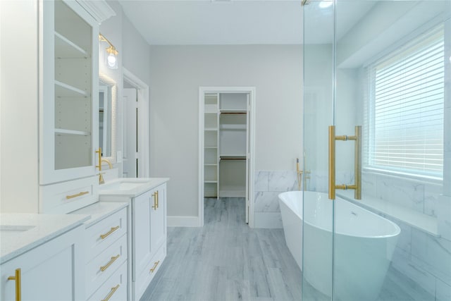 full bathroom with wood finished floors, a soaking tub, a walk in closet, and vanity