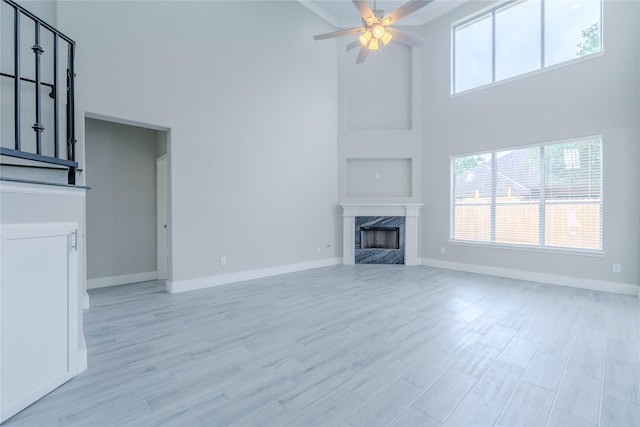 unfurnished living room featuring a fireplace, light wood-style floors, baseboards, ceiling fan, and a high ceiling