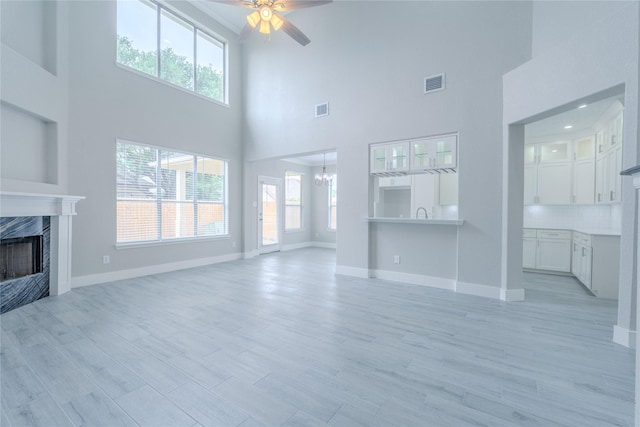 unfurnished living room with visible vents, a high end fireplace, ceiling fan with notable chandelier, a high ceiling, and a wealth of natural light