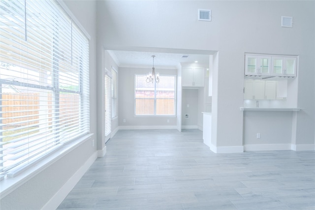 unfurnished living room featuring baseboards, a notable chandelier, light wood finished floors, and visible vents