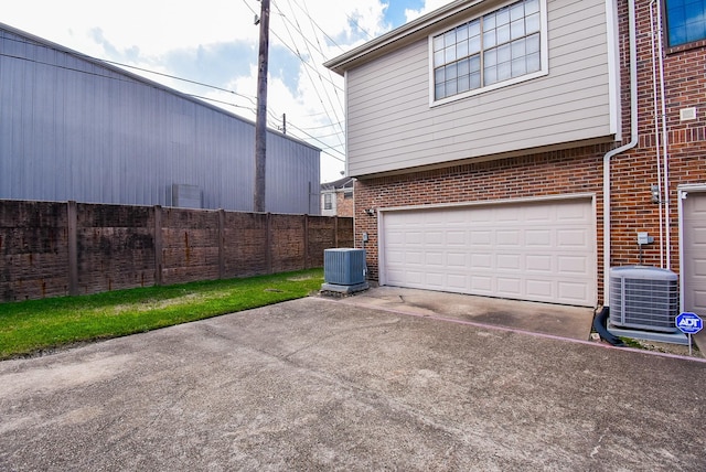 garage with central air condition unit, driveway, and fence