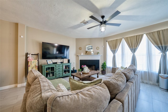 living area with a ceiling fan, a textured ceiling, visible vents, a tile fireplace, and baseboards