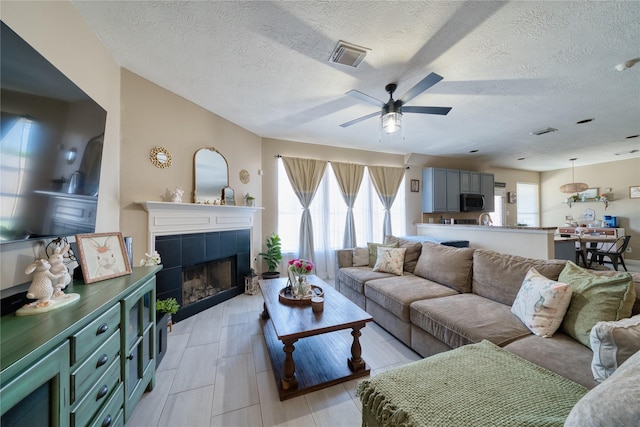 living area with visible vents, a ceiling fan, a healthy amount of sunlight, and a tile fireplace