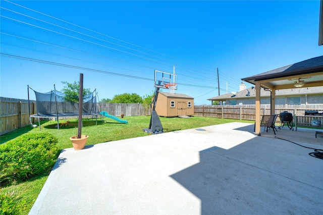 view of patio / terrace featuring ceiling fan, a trampoline, a storage shed, a fenced backyard, and an outdoor structure