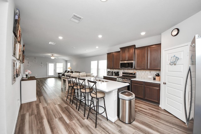 kitchen featuring appliances with stainless steel finishes, a breakfast bar area, light wood finished floors, and visible vents
