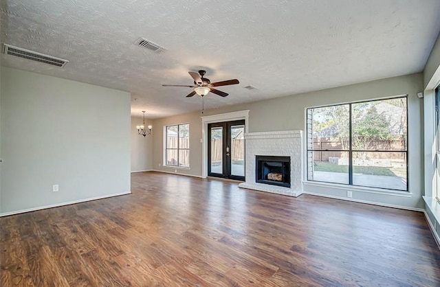 unfurnished living room featuring baseboards, ceiling fan with notable chandelier, dark wood finished floors, and visible vents
