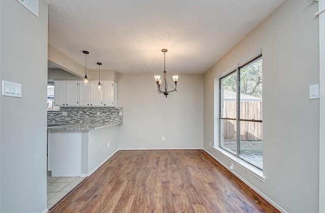 unfurnished dining area featuring baseboards, visible vents, wood finished floors, and a notable chandelier