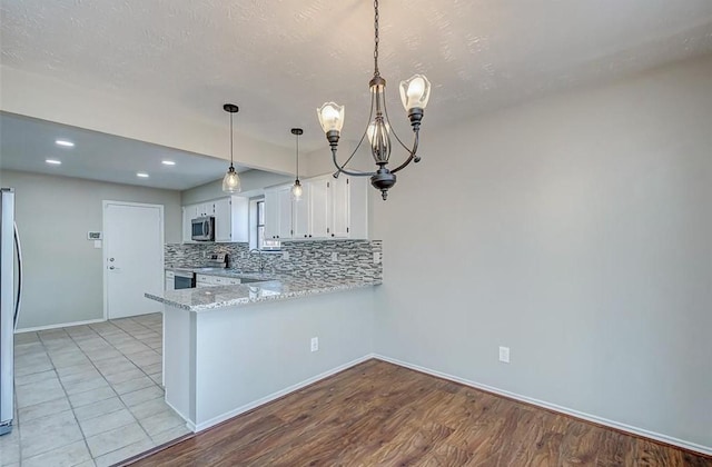 kitchen featuring backsplash, appliances with stainless steel finishes, white cabinets, a peninsula, and a chandelier