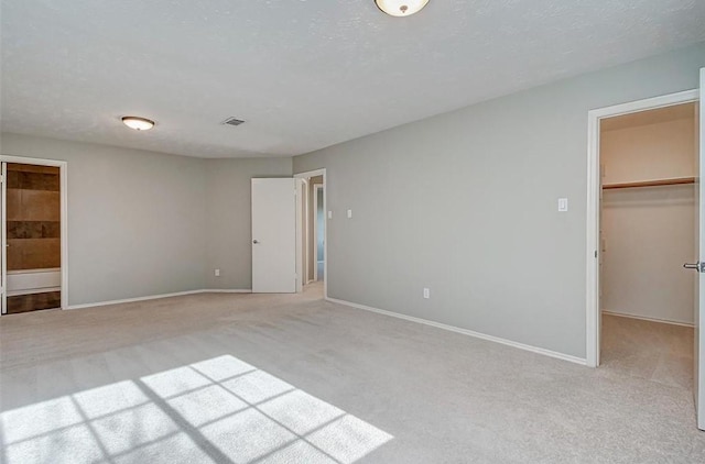 unfurnished bedroom featuring a closet, light carpet, baseboards, a walk in closet, and connected bathroom