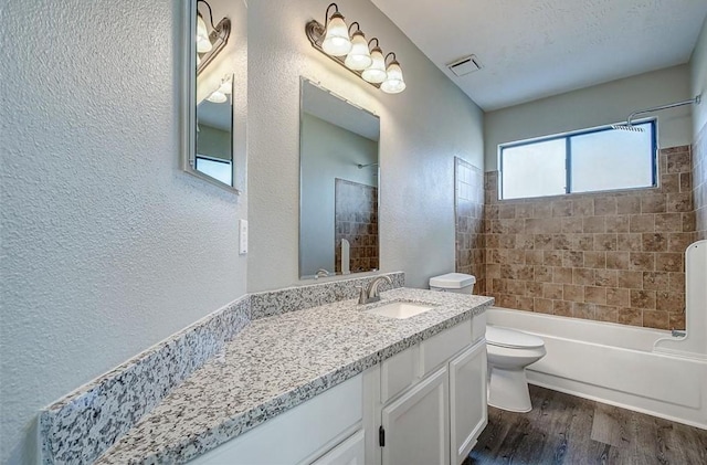 bathroom featuring a textured wall, wood finished floors, toilet, and shower / washtub combination