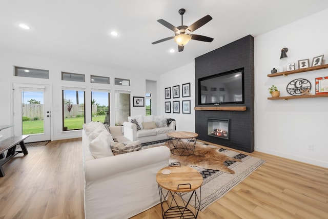 living room with a ceiling fan, light wood finished floors, and a fireplace