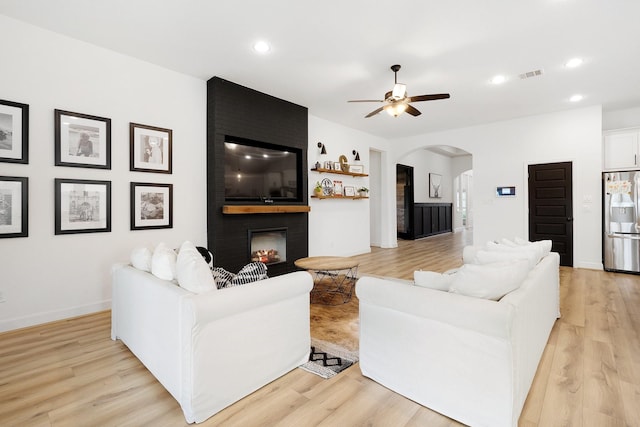living area featuring light wood-style floors, arched walkways, ceiling fan, and visible vents