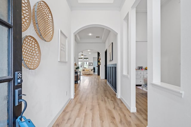 hallway featuring arched walkways, recessed lighting, light wood finished floors, and a raised ceiling