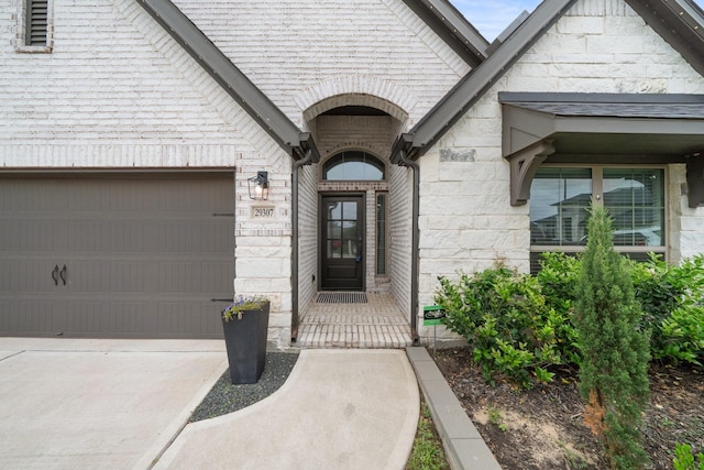 doorway to property featuring an attached garage, driveway, and stone siding