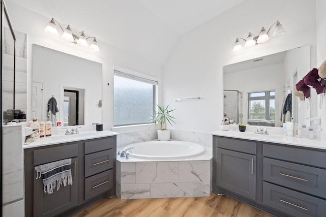 bathroom with a bath, a stall shower, wood finished floors, two vanities, and a sink