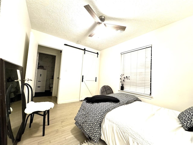 bedroom with a barn door, a textured ceiling, a ceiling fan, and light wood-style flooring