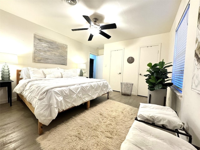 bedroom with two closets, baseboards, ceiling fan, and wood finished floors