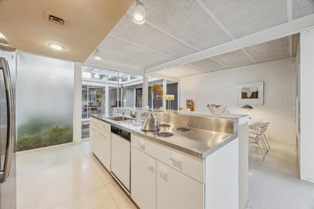 kitchen with white cabinets, a sink, dishwasher, brick wall, and visible vents