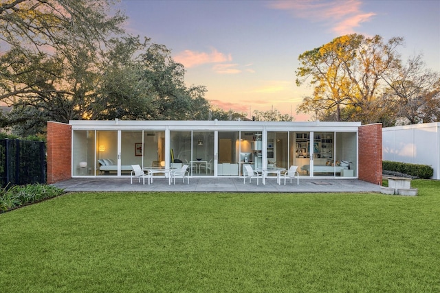 back of property at dusk with a lawn, a patio, fence, and a chimney