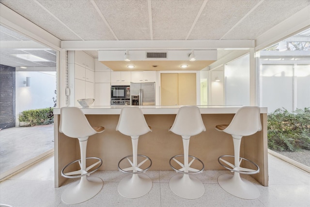 kitchen with a kitchen breakfast bar, black microwave, light countertops, stainless steel fridge with ice dispenser, and white cabinetry
