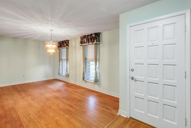 foyer featuring baseboards, light wood finished floors, a textured ceiling, and a notable chandelier