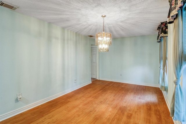 unfurnished dining area featuring visible vents, baseboards, a textured ceiling, a chandelier, and light wood-style flooring