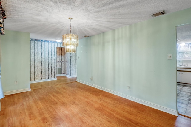 unfurnished dining area featuring visible vents, light wood-style floors, baseboards, a sink, and a notable chandelier