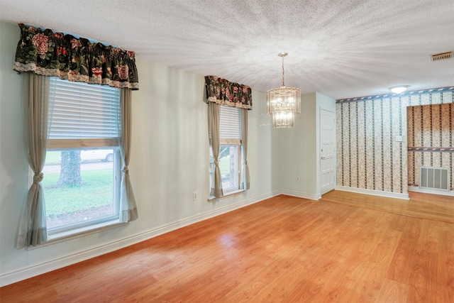 unfurnished dining area featuring a chandelier, baseboards, visible vents, and wood finished floors