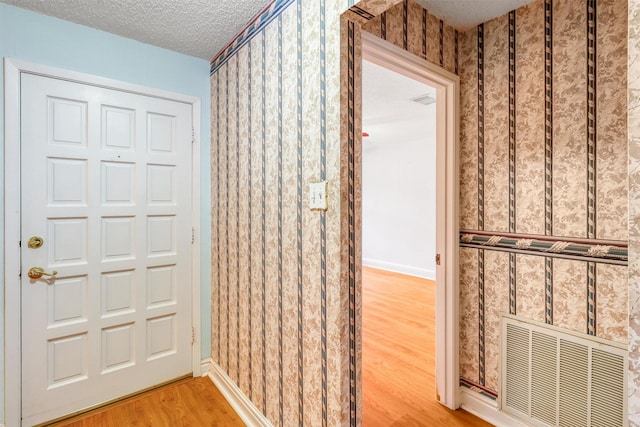 interior space with baseboards, light wood finished floors, a textured ceiling, and visible vents