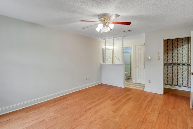 unfurnished room featuring ceiling fan, a textured ceiling, light wood-style flooring, baseboards, and visible vents