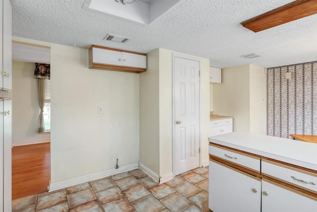 kitchen with light countertops, a textured ceiling, white cabinetry, baseboards, and visible vents