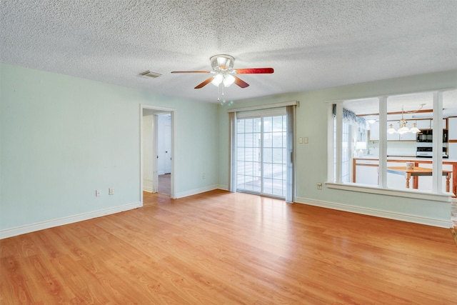 empty room featuring visible vents, light wood-style floors, baseboards, ceiling fan, and a textured ceiling