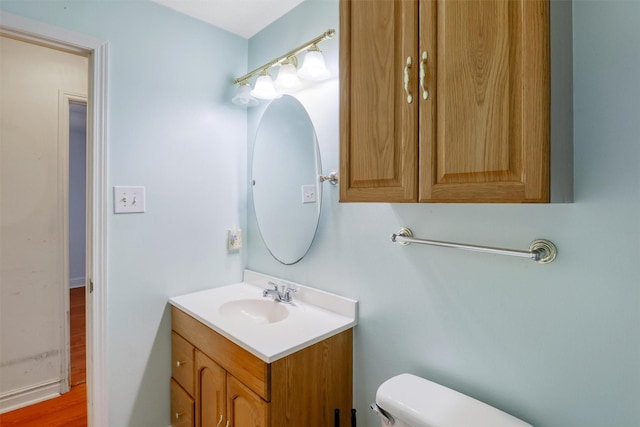 half bath with vanity, wood finished floors, and toilet