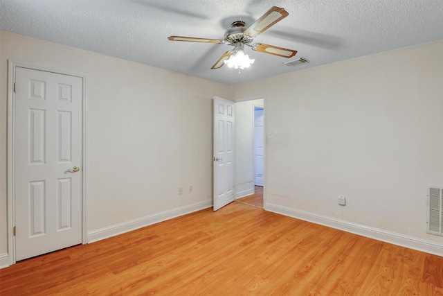 empty room with ceiling fan, a textured ceiling, visible vents, light wood-type flooring, and baseboards
