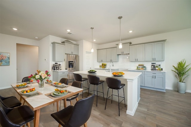 kitchen with a breakfast bar area, stainless steel refrigerator with ice dispenser, tasteful backsplash, a center island with sink, and light wood-type flooring