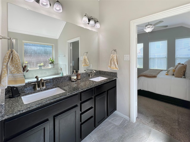 ensuite bathroom featuring baseboards, vaulted ceiling, and a sink