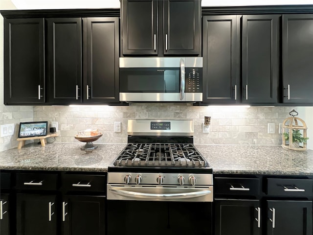 kitchen featuring stainless steel appliances, light stone counters, dark cabinets, and tasteful backsplash