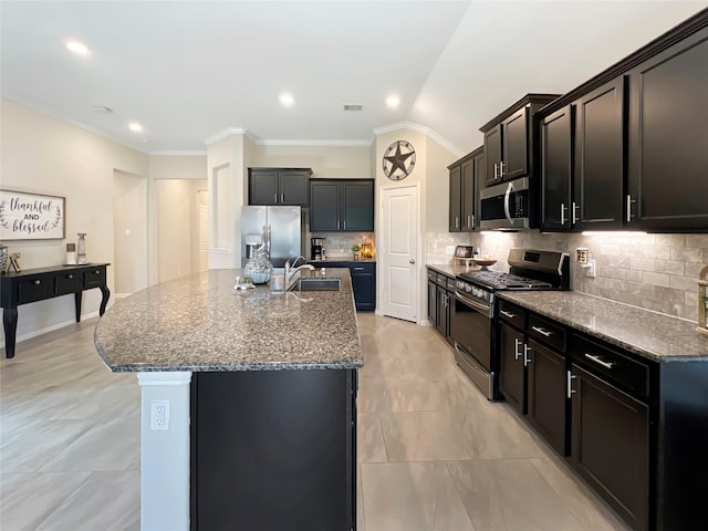 kitchen featuring decorative backsplash, a kitchen island with sink, a sink, dark stone countertops, and stainless steel appliances