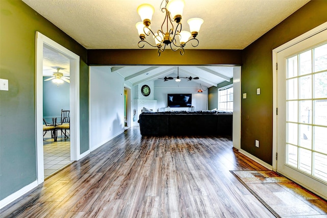 living area with baseboards, vaulted ceiling with beams, ceiling fan with notable chandelier, and wood finished floors