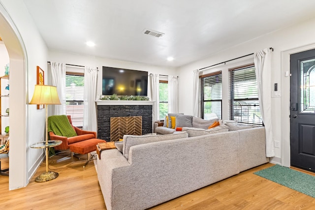 living area featuring visible vents, arched walkways, a fireplace, baseboards, and light wood-style flooring