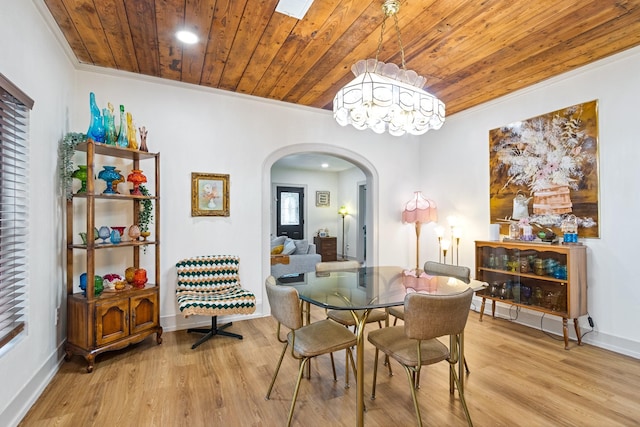 dining area featuring crown molding, light wood-style floors, baseboards, wooden ceiling, and arched walkways